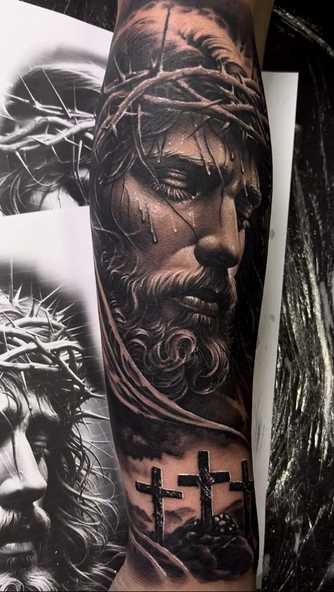 Jesus com coroa de espinhos e três cruzes em realismo no braço